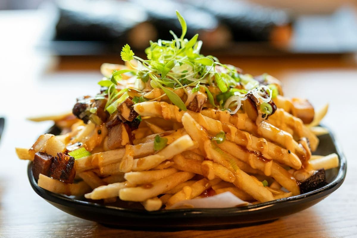 Bord friet met gebakken stukjes, saus en verse kiemgroente